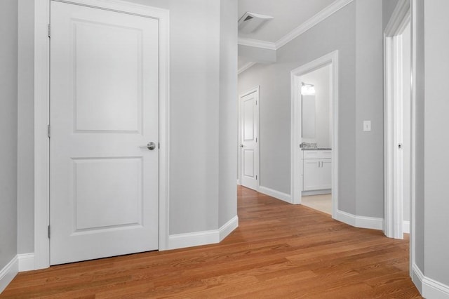 hallway featuring light wood-style floors, visible vents, ornamental molding, and baseboards