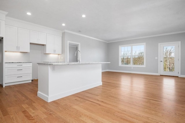 kitchen featuring light wood finished floors, baseboards, white cabinets, an island with sink, and crown molding