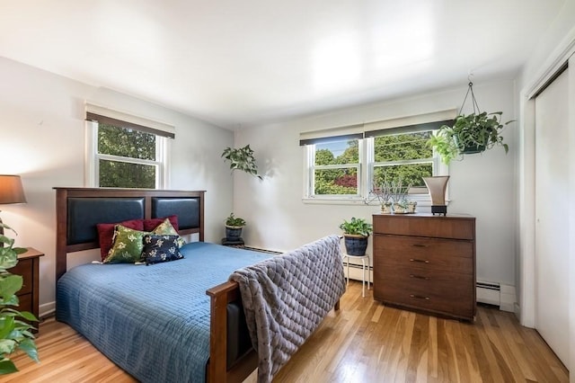 bedroom with multiple windows, wood finished floors, and baseboard heating