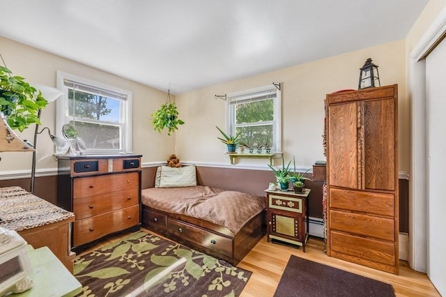 bedroom featuring multiple windows, light wood-style floors, and a baseboard heating unit