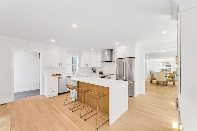 kitchen featuring a kitchen island, a breakfast bar area, wall chimney range hood, a sink, and appliances with stainless steel finishes