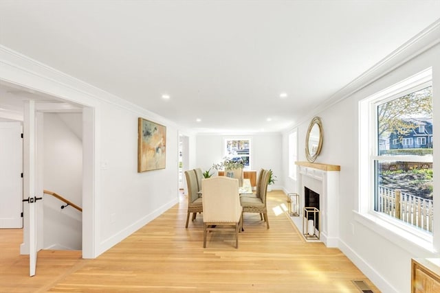 dining area with light wood-style floors, ornamental molding, a fireplace with flush hearth, and visible vents