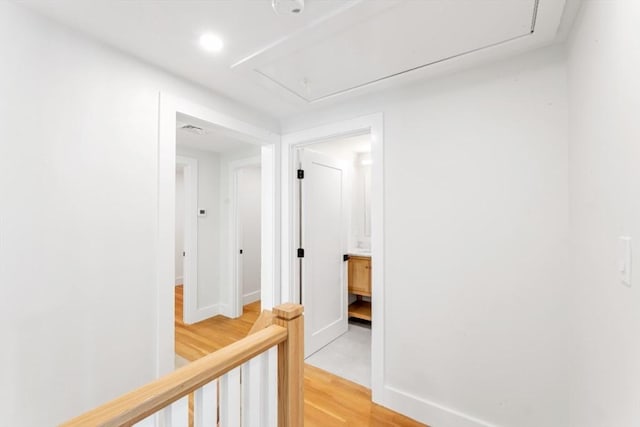 hall with attic access, visible vents, light wood-type flooring, baseboards, and recessed lighting