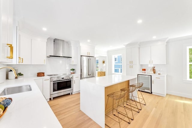 kitchen featuring wall chimney range hood, a sink, light wood-style floors, a kitchen breakfast bar, and stainless steel appliances