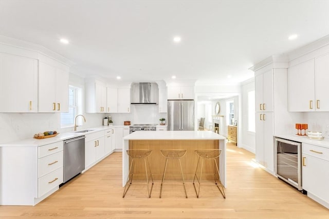 kitchen with a kitchen island, a sink, beverage cooler, stainless steel appliances, and wall chimney exhaust hood