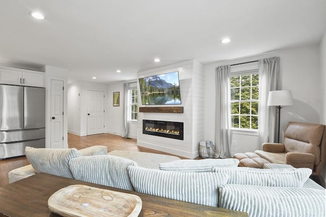 living room featuring light wood finished floors, baseboards, a glass covered fireplace, and recessed lighting