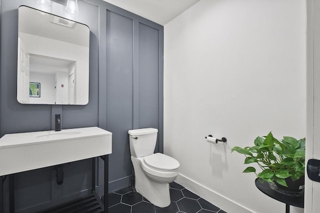 half bath with tile patterned flooring, baseboards, a sink, and toilet