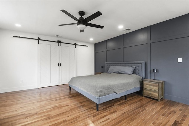 bedroom featuring visible vents, a decorative wall, light wood finished floors, and a barn door