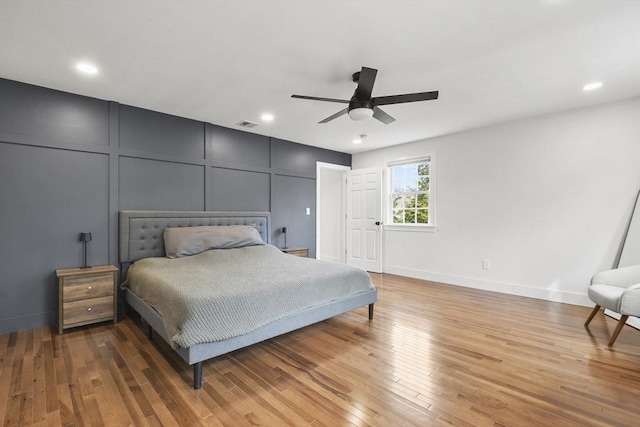 bedroom featuring ceiling fan, a decorative wall, wood finished floors, and recessed lighting