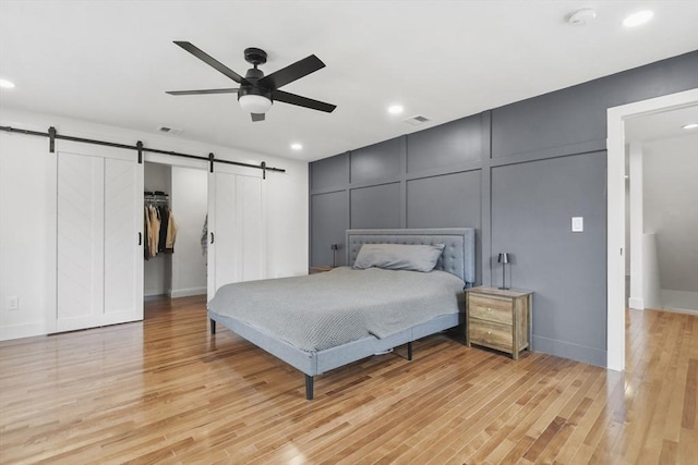 bedroom with a barn door, visible vents, a decorative wall, and light wood-style flooring