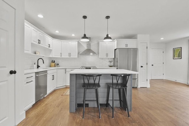 kitchen featuring light wood-style floors, appliances with stainless steel finishes, light countertops, wall chimney range hood, and a sink