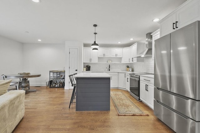 kitchen featuring a center island, light wood finished floors, stainless steel appliances, white cabinetry, and wall chimney exhaust hood