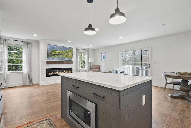 kitchen featuring light wood-type flooring, a glass covered fireplace, gray cabinets, and stainless steel microwave