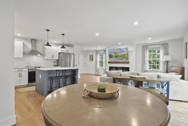 dining space with a lit fireplace, light wood-style flooring, and recessed lighting