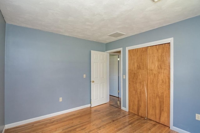 unfurnished bedroom featuring baseboards, wood finished floors, and a closet