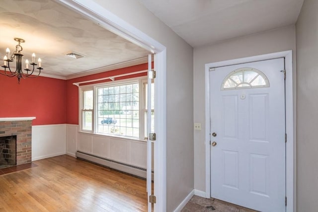 foyer entrance with visible vents, wood finished floors, a fireplace, a baseboard heating unit, and a chandelier