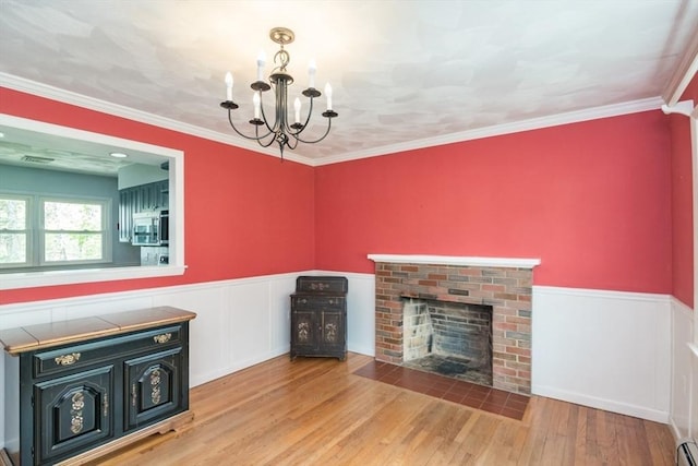 unfurnished living room with wainscoting, a brick fireplace, a chandelier, and baseboard heating