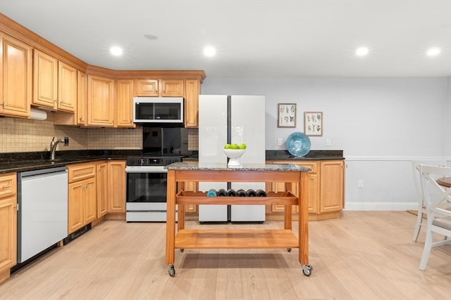 kitchen with stainless steel dishwasher, range, light hardwood / wood-style floors, and dark stone counters