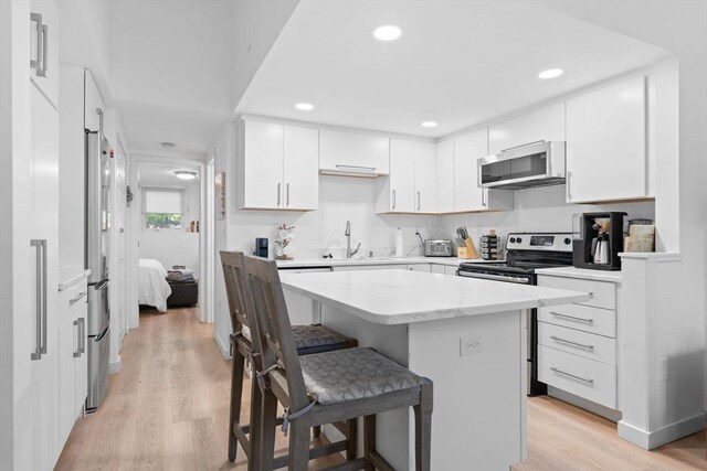2A Brewer St, Boston, MA 02130 - kitchen with appliances with stainless steel finishes, a sink, a kitchen bar, light wood-type flooring, and white cabinets