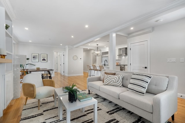 living room with ornamental molding, sink, light hardwood / wood-style floors, and a notable chandelier