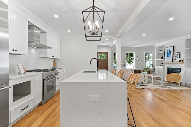 kitchen featuring wall chimney range hood, stainless steel stove, decorative light fixtures, light hardwood / wood-style floors, and white cabinetry