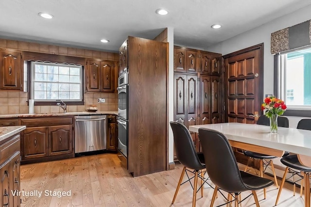 kitchen featuring light countertops, light wood-style floors, stainless steel dishwasher, and tasteful backsplash