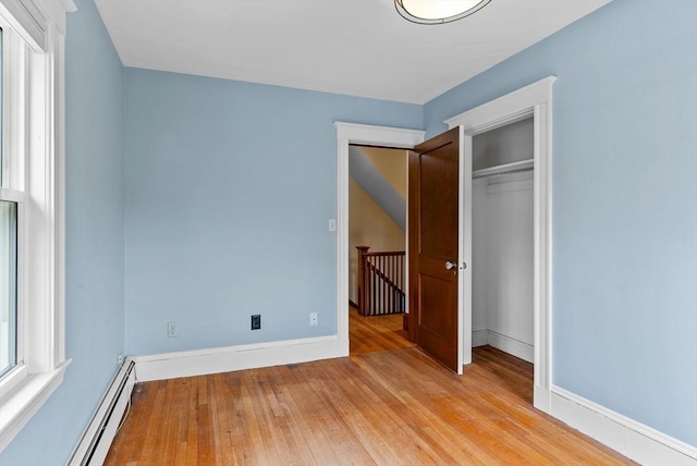 unfurnished bedroom with baseboards, light wood-type flooring, baseboard heating, and a closet