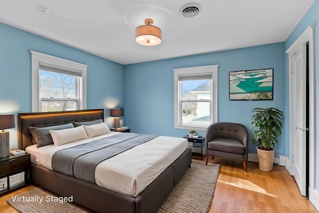 bedroom with light wood-style flooring, a baseboard heating unit, visible vents, and multiple windows