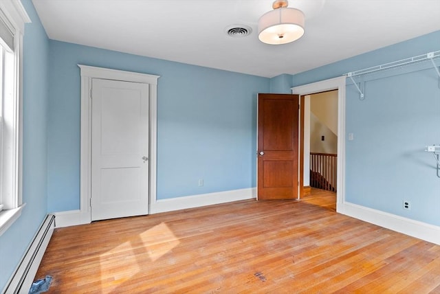 unfurnished bedroom with a baseboard heating unit, baseboards, visible vents, and light wood-type flooring