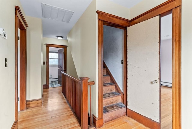 hallway with a baseboard heating unit, an upstairs landing, visible vents, light wood finished floors, and baseboards