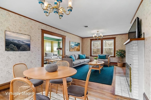 interior space with wood finished floors, wallpapered walls, a fireplace, a notable chandelier, and ornamental molding