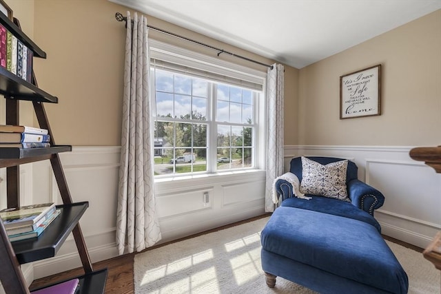 sitting room with wood finished floors, a wainscoted wall, and a decorative wall