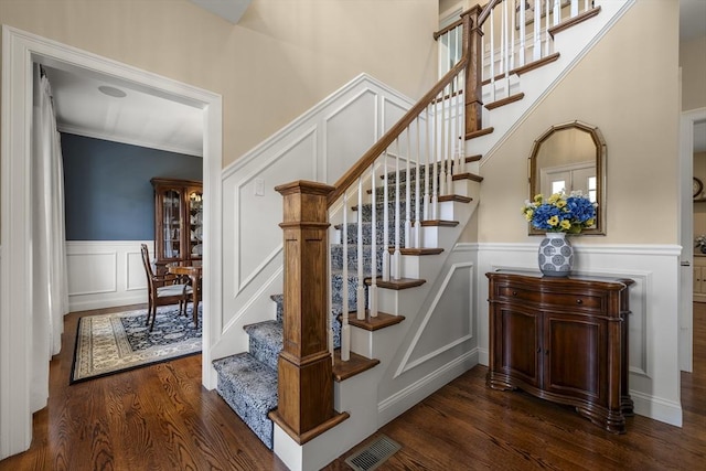 stairway featuring visible vents, wainscoting, wood finished floors, and a decorative wall