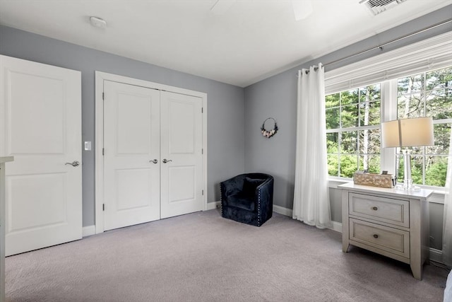 living area with visible vents, a wealth of natural light, light carpet, and baseboards