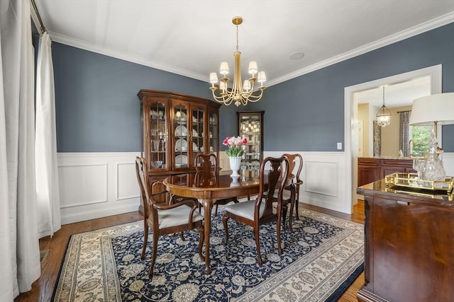dining room featuring a chandelier, wood finished floors, a wainscoted wall, and ornamental molding