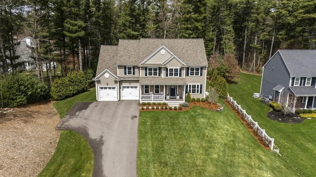 colonial house with covered porch, fence, aphalt driveway, a garage, and a front lawn