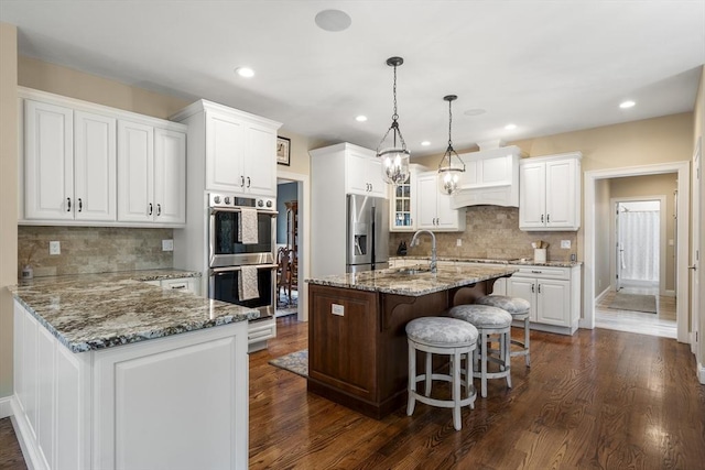 kitchen with a kitchen breakfast bar, white cabinetry, tasteful backsplash, a sink, and appliances with stainless steel finishes