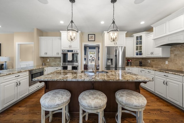 kitchen with glass insert cabinets, decorative backsplash, appliances with stainless steel finishes, a sink, and white cabinetry