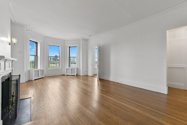 unfurnished living room featuring plenty of natural light, a fireplace, hardwood / wood-style flooring, radiator, and crown molding