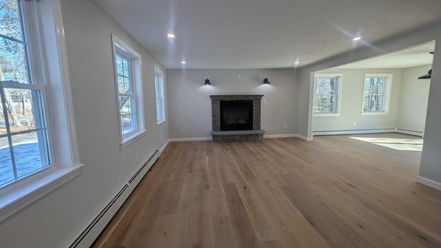 unfurnished living room featuring baseboards, a fireplace with raised hearth, baseboard heating, and wood finished floors