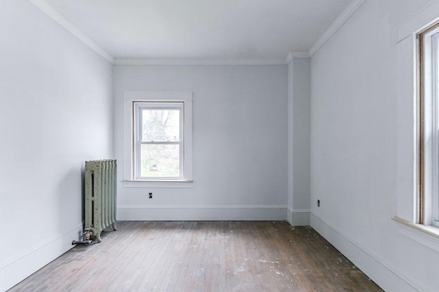 empty room featuring hardwood / wood-style floors, baseboards, crown molding, and radiator