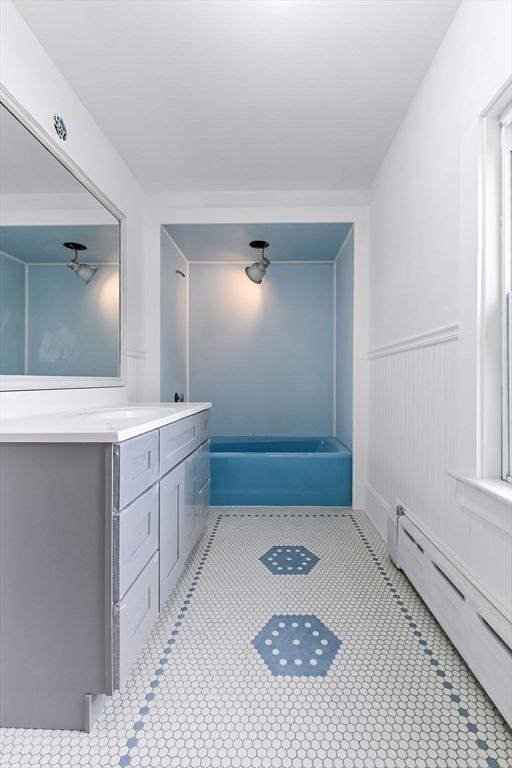 full bathroom with baseboard heating, a bath, tile patterned floors, vanity, and wainscoting