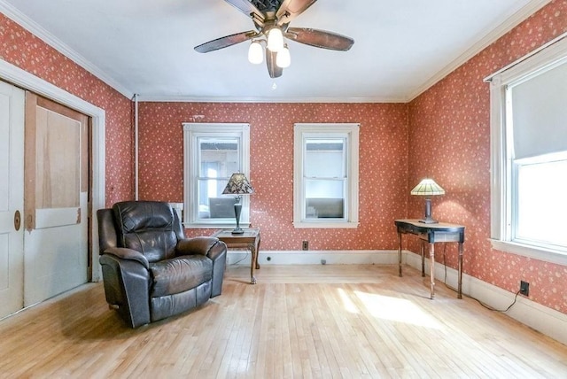 living area with hardwood / wood-style floors, wallpapered walls, ornamental molding, and ceiling fan