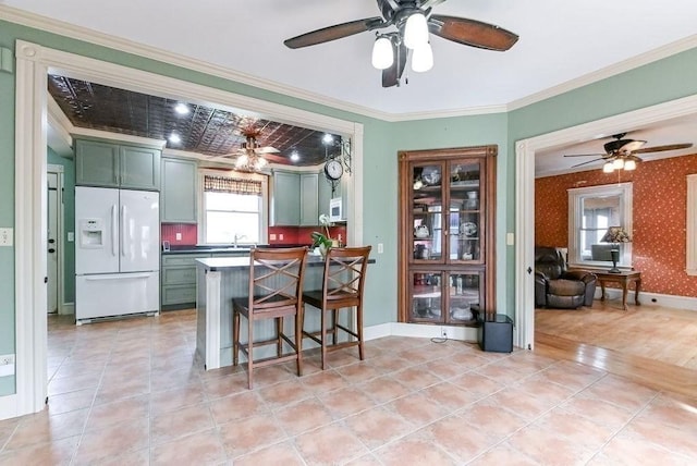 kitchen featuring white fridge with ice dispenser, a ceiling fan, green cabinetry, and crown molding