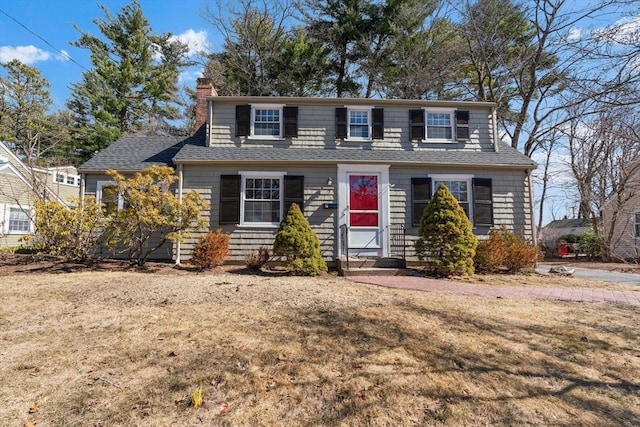 view of front of house featuring a front yard, a chimney, and a shingled roof