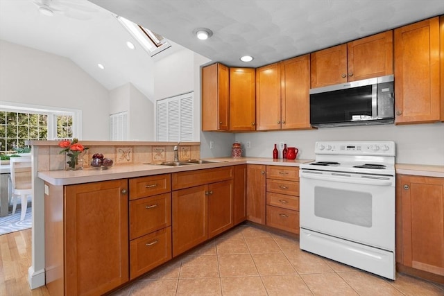 kitchen featuring stainless steel microwave, light countertops, a peninsula, electric stove, and a sink