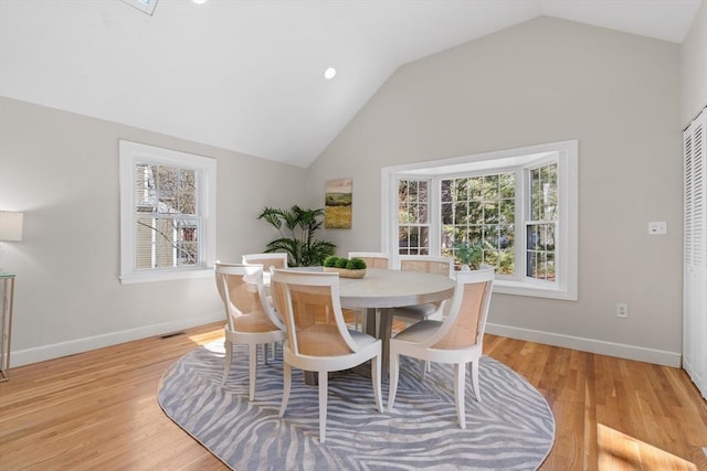 dining room featuring light wood-type flooring, baseboards, visible vents, and vaulted ceiling