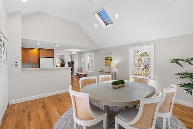 dining area with high vaulted ceiling, light wood-style flooring, recessed lighting, a skylight, and baseboards