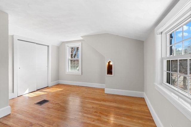 additional living space with light wood-type flooring, visible vents, baseboards, and lofted ceiling