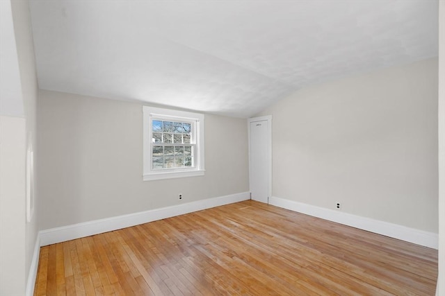 empty room featuring light wood-type flooring, lofted ceiling, and baseboards